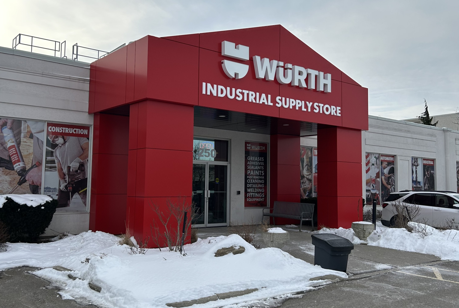 A Würth Industrial Supply Store exterior with a bold red entrance structure and white signage. Snow covers the ground around the building, with product graphics on the walls and parked vehicles visible nearby.